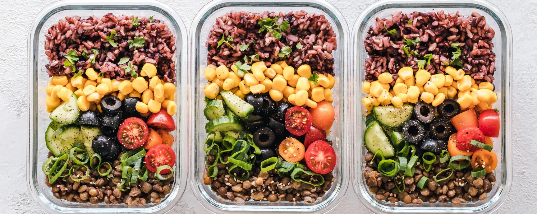3 trays with a colourfull meal including tomato, lentils, corn, rice and some veggies